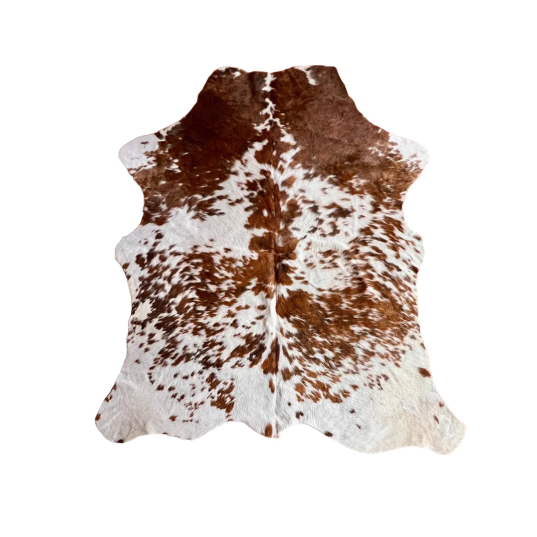 A natural brown and white cowhide rug laid flat on a brown tiled floor, showing a natural spotted pattern with a darker brown venter and a white shoulder.
