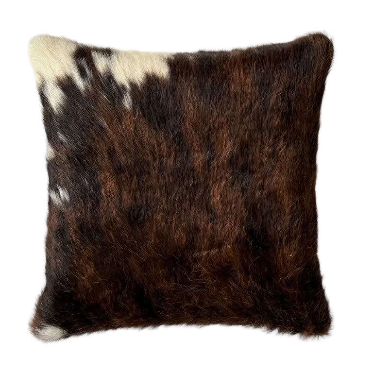 A cushion cowhide throw pillow with a dark brown and black pattern and white patches,