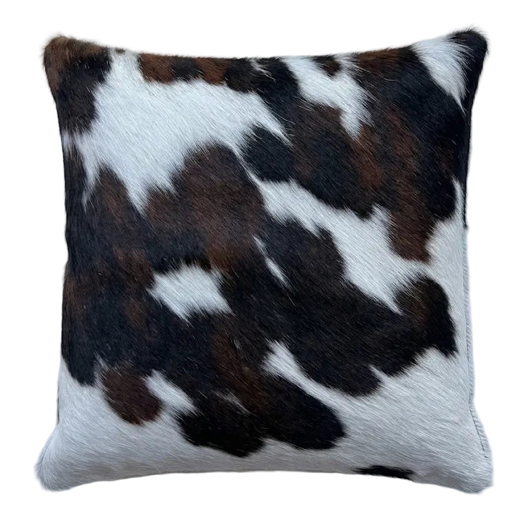 A square cushion made of cowhide with a natural black, brown, and white spotted pattern,