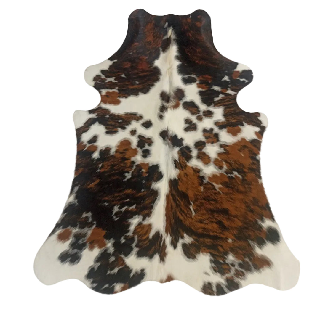 A natural cowhide rug with a brown, black, and white mottled pattern, laid flat on a light-colored surface.