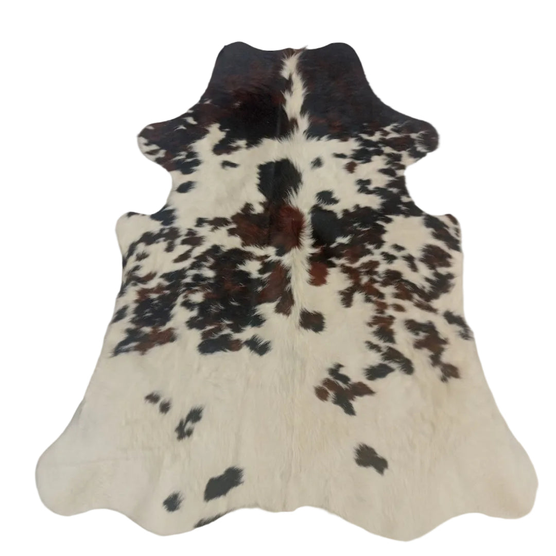 A natural cowhide rug with a black and white spotted pattern and some reddish-brown patches, laid flat on a light-colored surface.
