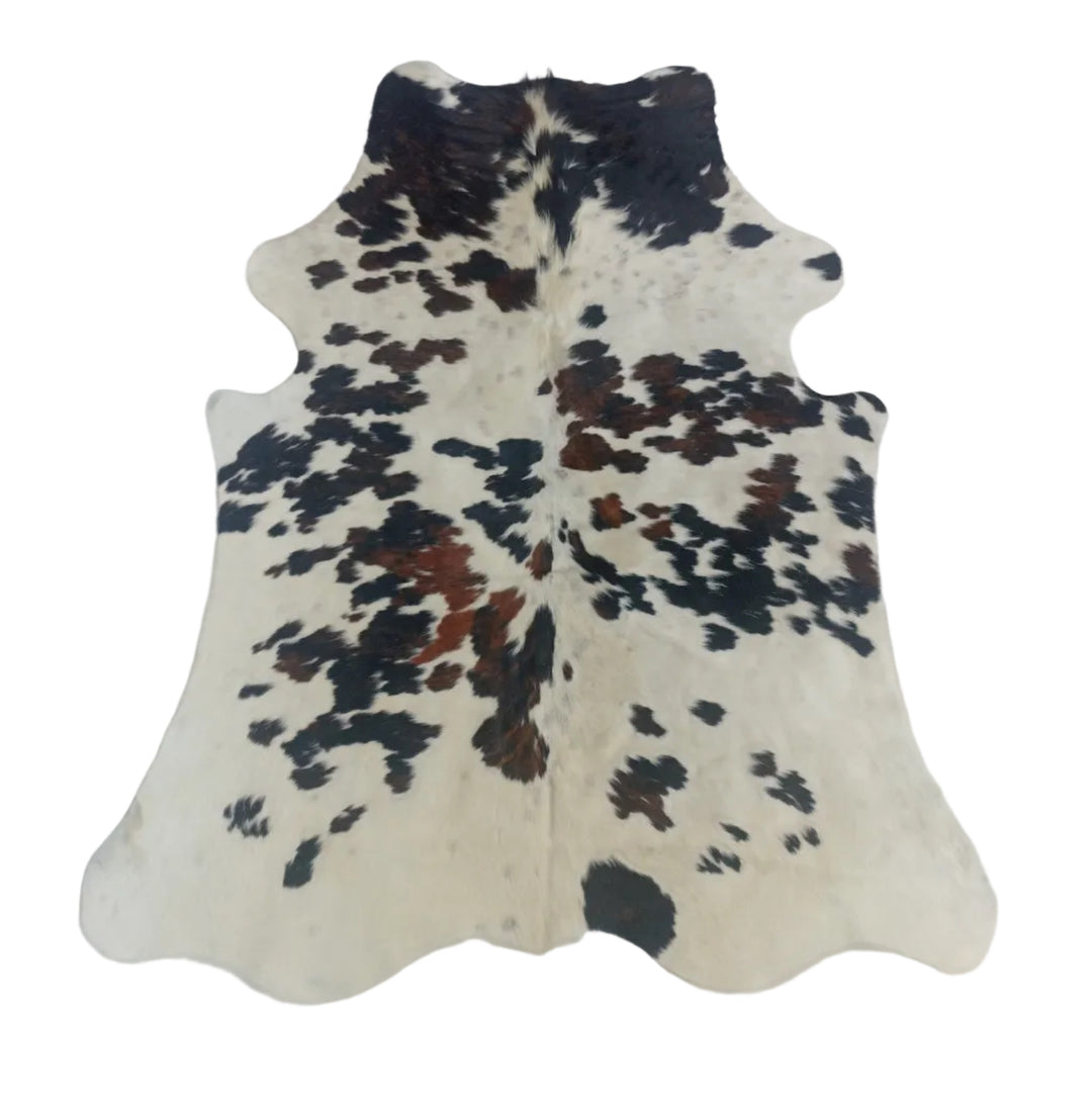 A natural cowhide rug with a black and brown spotted pattern on an off-white base, laid flat on a light-colored surface.
