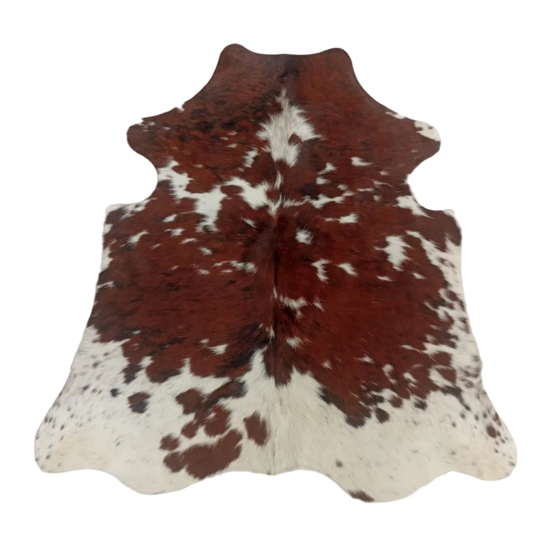 A natural cowhide rug with a brown and white spotted pattern, laid flat on a light-colored fabric surface.