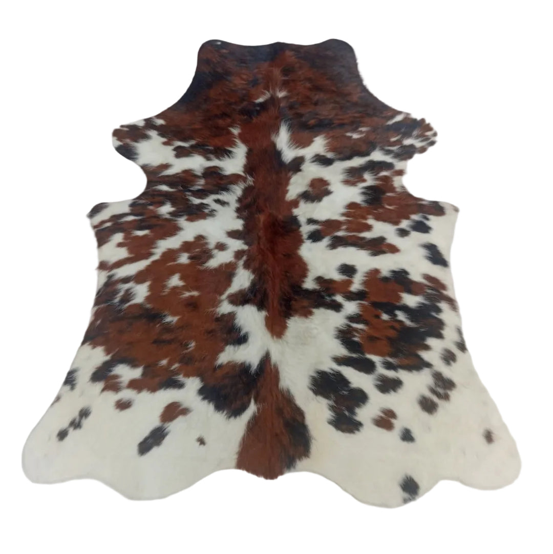 A natural cowhide rug with a brown, black, and white spotted pattern, laid flat on a light-colored surface.