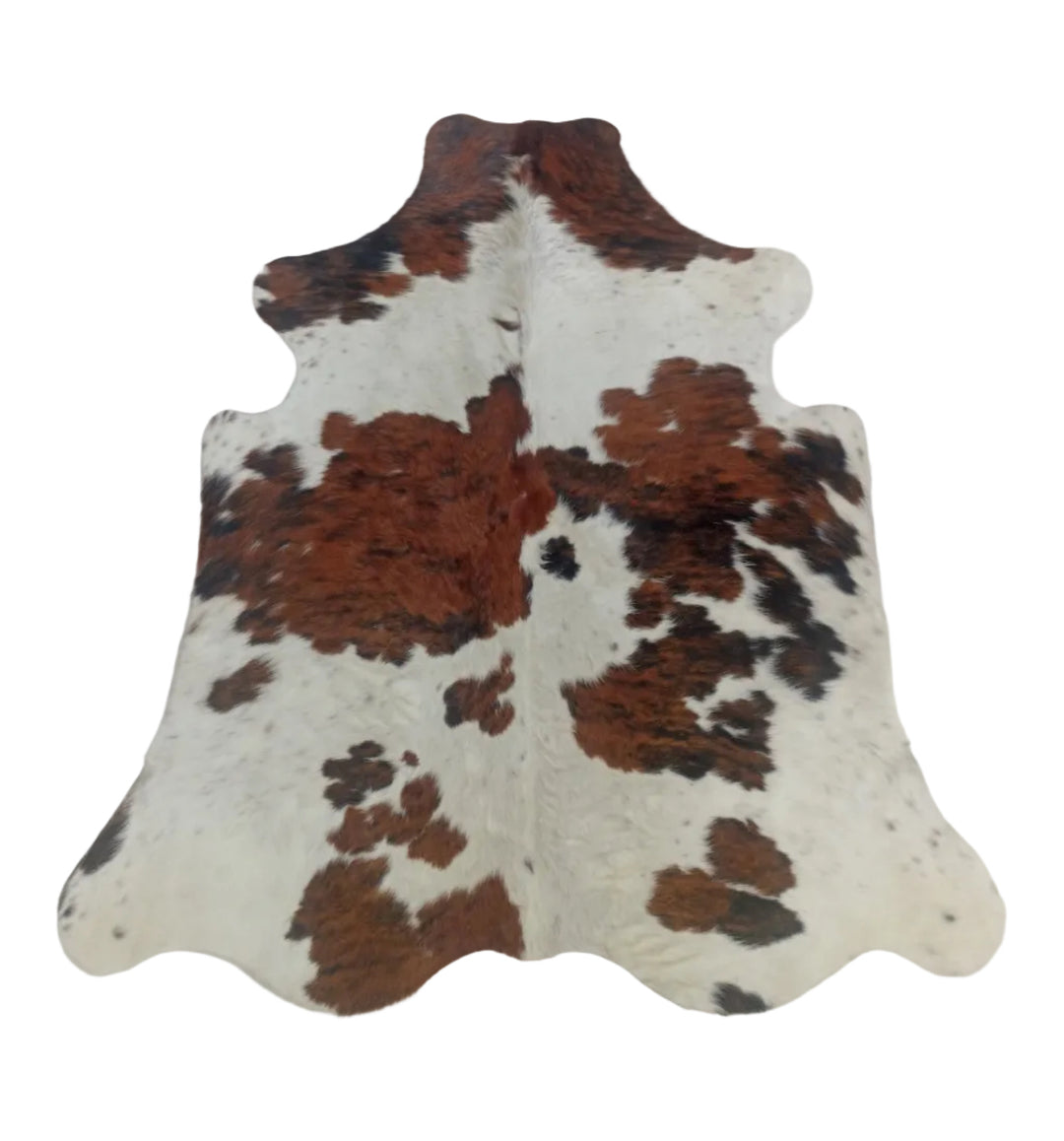 A natural cowhide rug with a brown and black spotted pattern on an off-white base, laid flat on a light-colored floor.