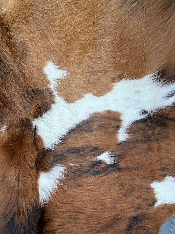 Brown and white cowhide fur rug  close-up showing natural spotted pattern and soft texture.