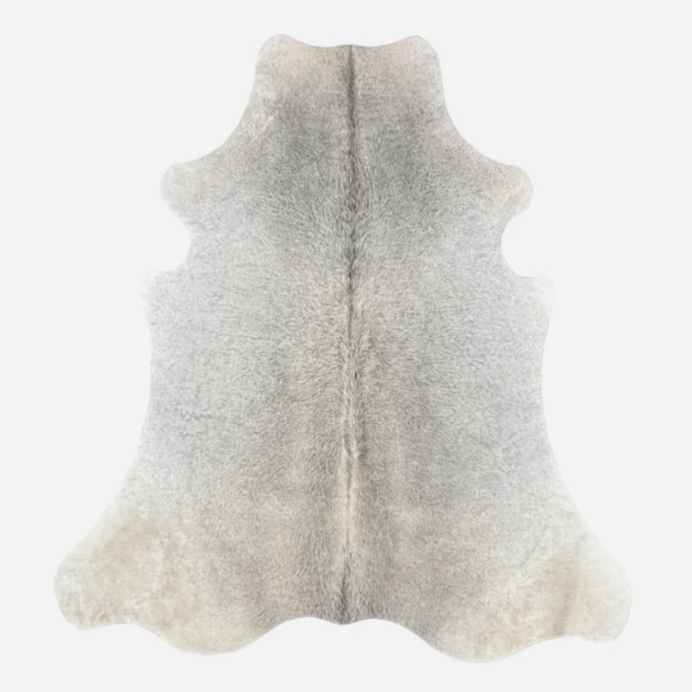A natural cowhide rug with a curly fur texture, featuring a light gray center that fades to warm cream and beige at the rounded edges, shown against a plain white background.