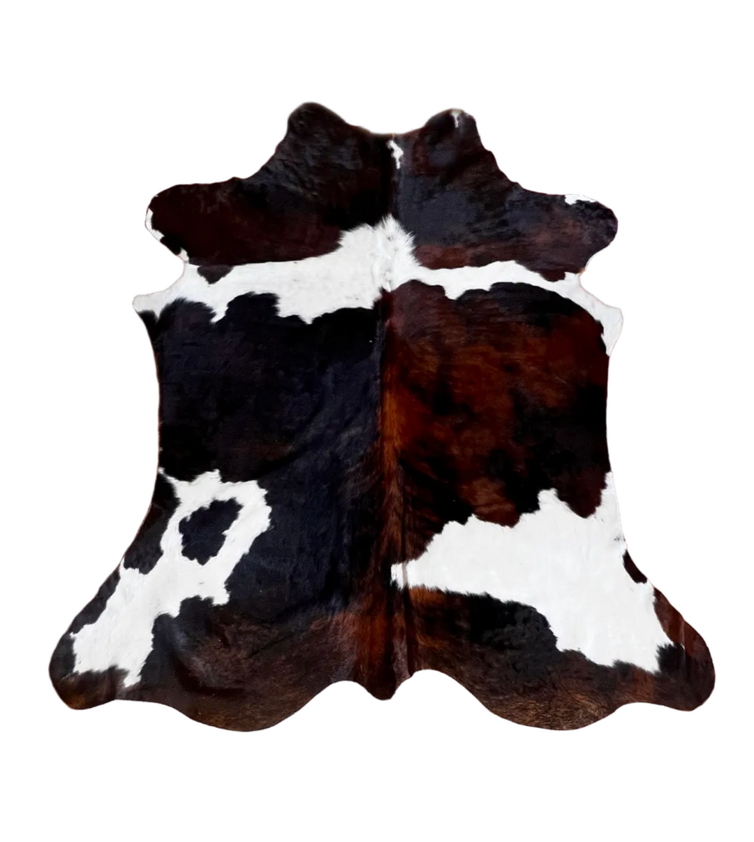 A natural cowhide rug with a black and white spotted pattern, laid flat on a brown tiled floor.