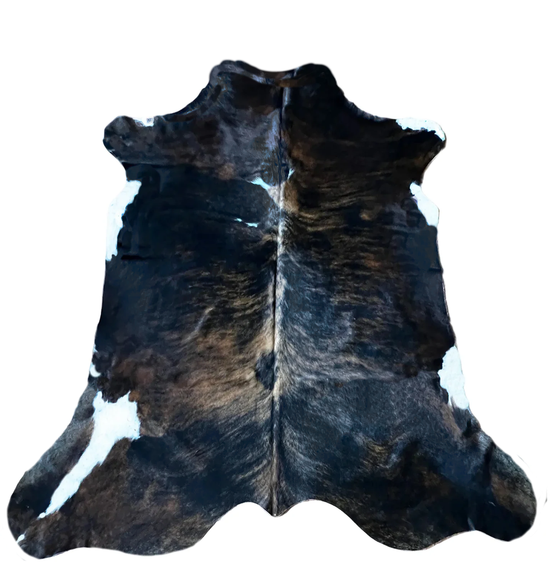 A natural cowhide rug with a dark brown and black base, featuring prominent white patches and a central hairline, 