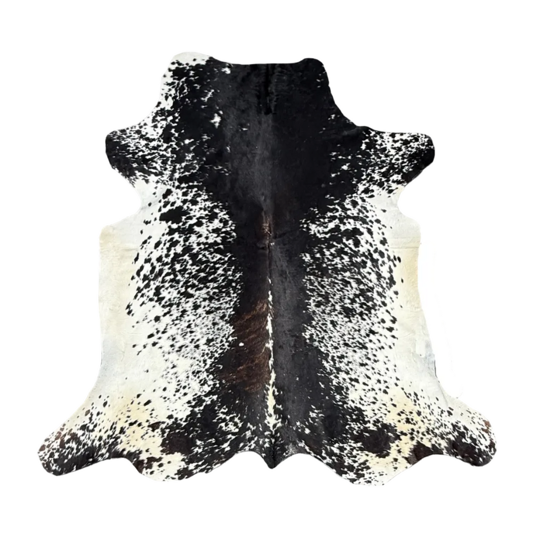 A natural black and white cowhide rug laid flat on a gray wooden deck, with a r.