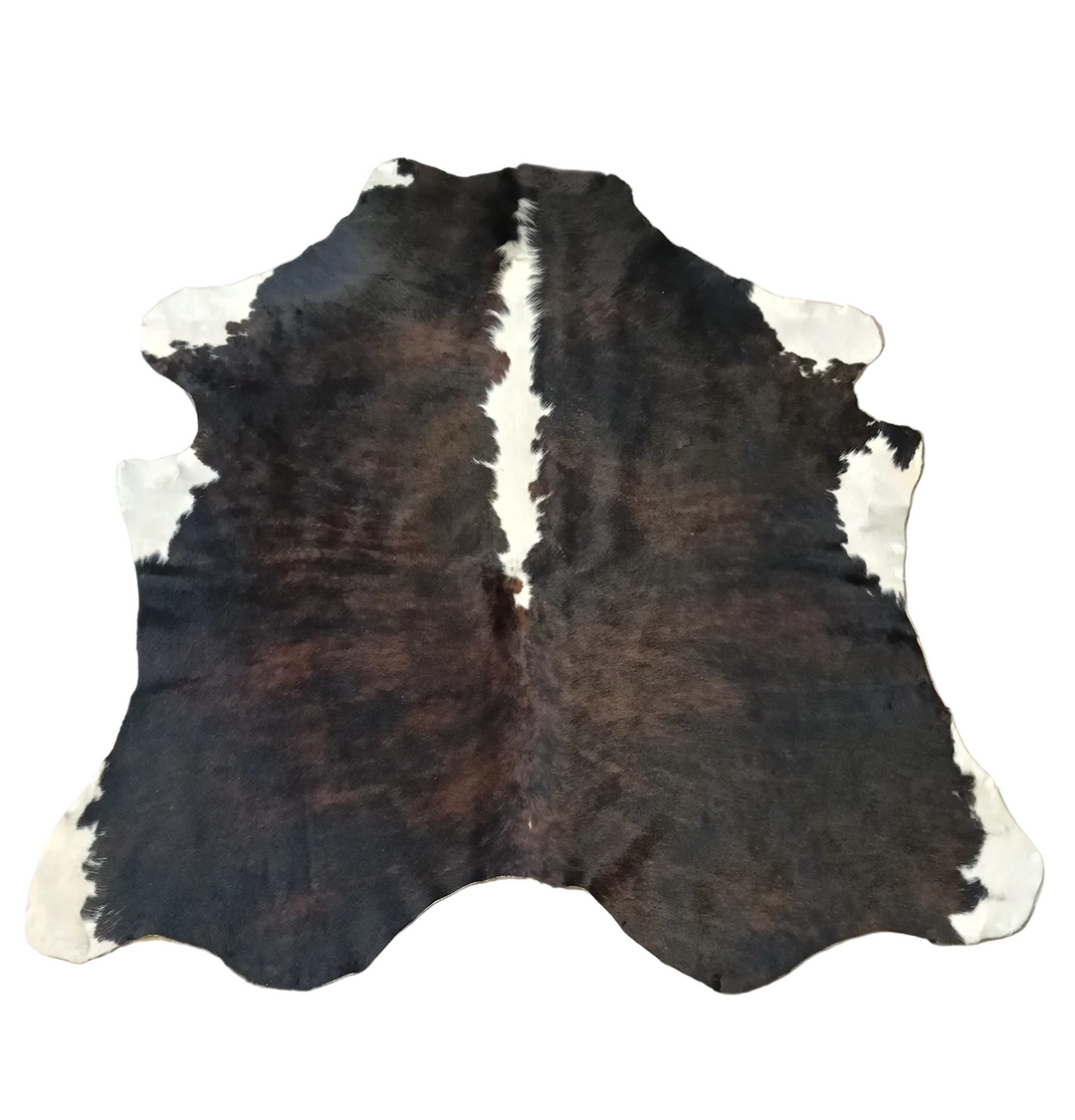 A natural cowhide rug with a dark brown and black spotted pattern, a white center stripe, and white patches on the sides, 