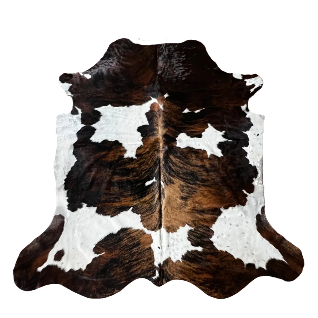 A natural cowhide rug with a classic black and white spotted pattern, featuring a central white stripe and dark brown edges, shown flat against a white background.