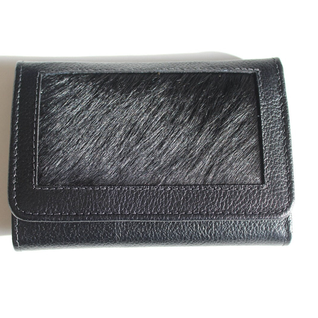 A black leather wallet with a textured pebbled finish and a central rectangular patch of black and gray hair-on-hide, shown on a white background with a soft shadow.
